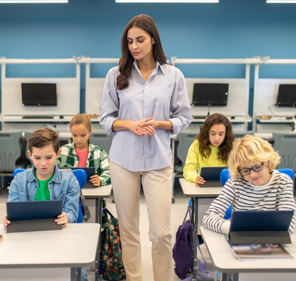woman standing watching students working tablets
